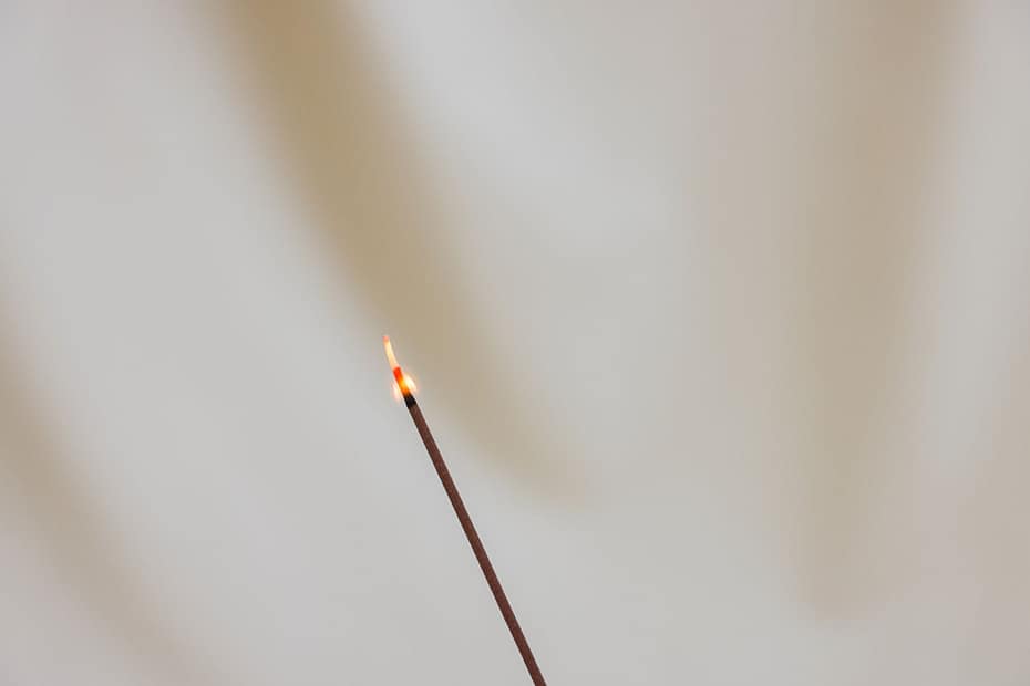 Hand-rolled herbal incense stick with gentle smoke rising on a calm, natural linen background