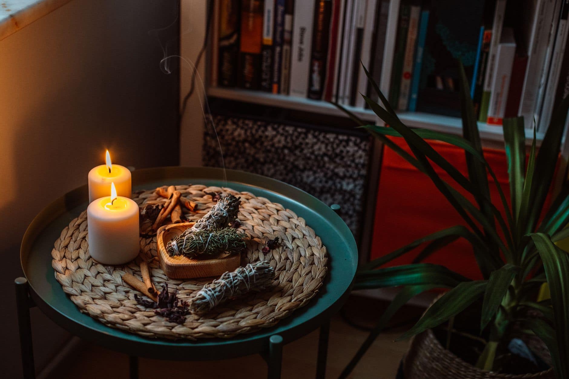 Incense burning in a calm, candle-lit corner of a home with a plant nearby