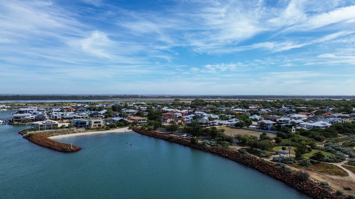 A coastal town from the air, houses and streets gathered around a sheltered inlet with a marina along one edge.